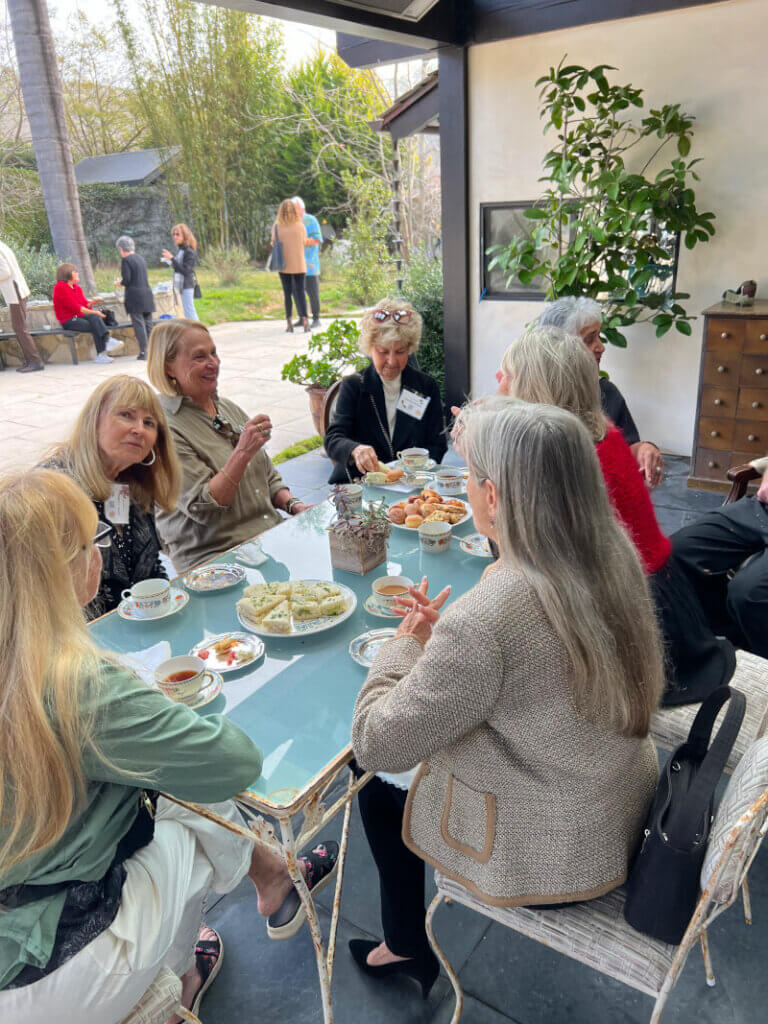 Guests outside sitting at a table enjoying conversation while sipping tea and enjoying lovely edibles,