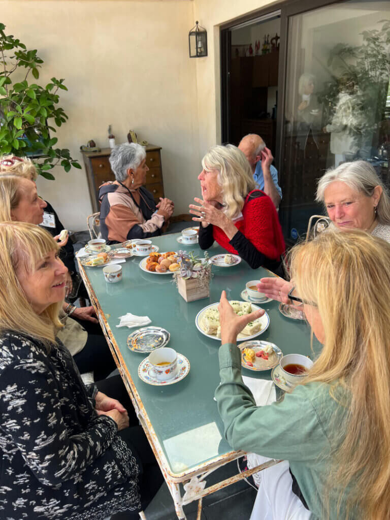 Guests outside sitting at a table enjoying conversation while sipping tea and enjoying lovely edibles,