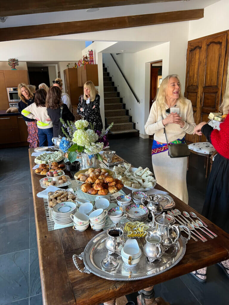 Attendees standing near a table filled with tea cakes and other delectables.